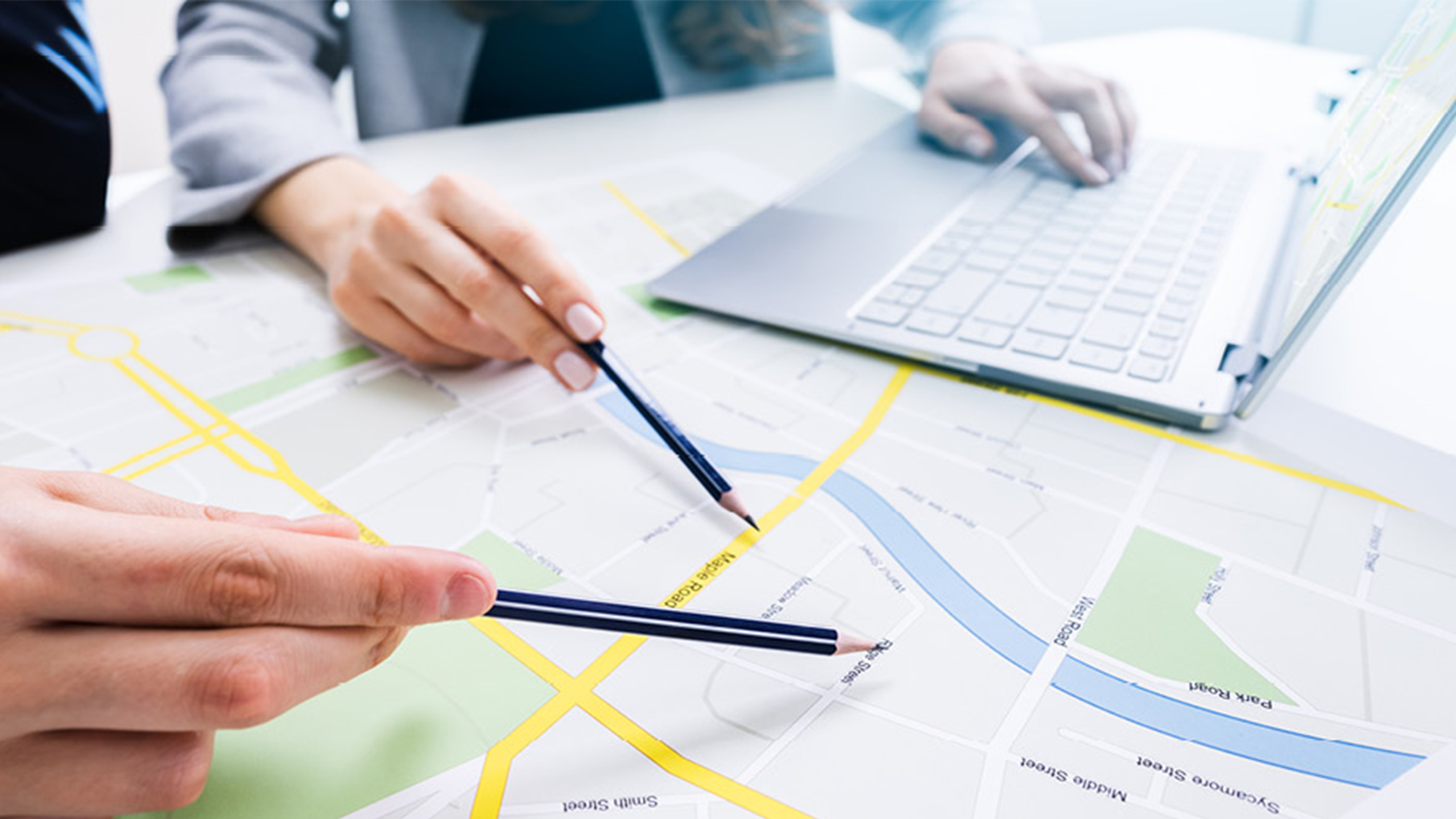Zwei Personen arbeiten gemeinsam an einem Stadtplan und Laptop – visuelle Darstellung strategischer Planung und Kommunikation der Veränderung in Städten und Gemeinden.
