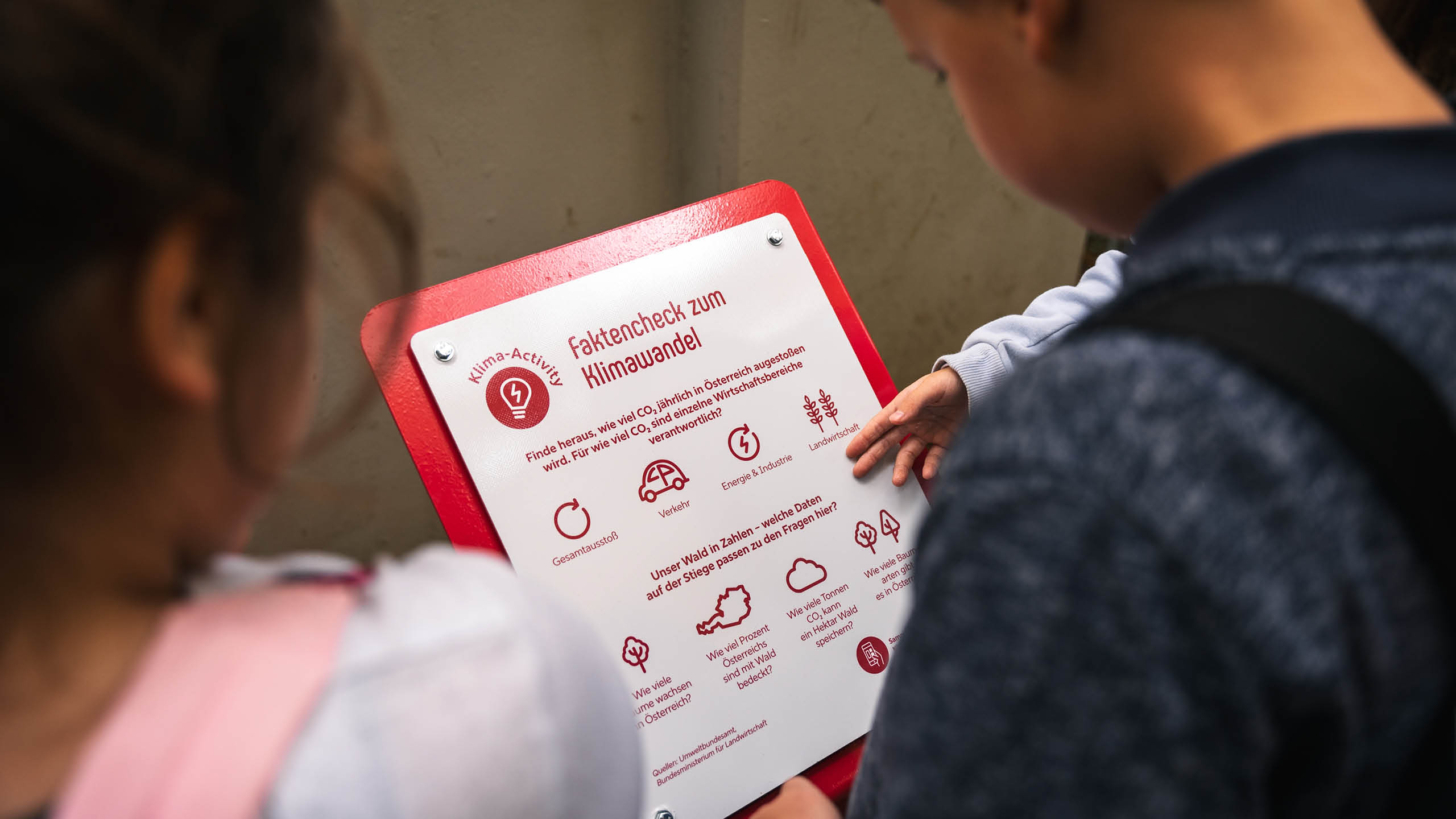 Kinder an einer Lernstation des KlimaWaldWeg Hainfeld beim Faktencheck zum Klimawandel mit Symbolen zu Verkehr, Energie, Wald und CO₂-Ausstoß.