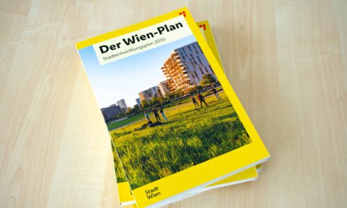 Gedruckte Broschüre des Wien-Plans – Stadtentwicklungsplan 2035 – mit gelbem Einband, einem Foto von Menschen auf einer Wiese vor Wohngebäuden und dem Logo der Stadt Wien, liegend auf einem hellen Holztisch