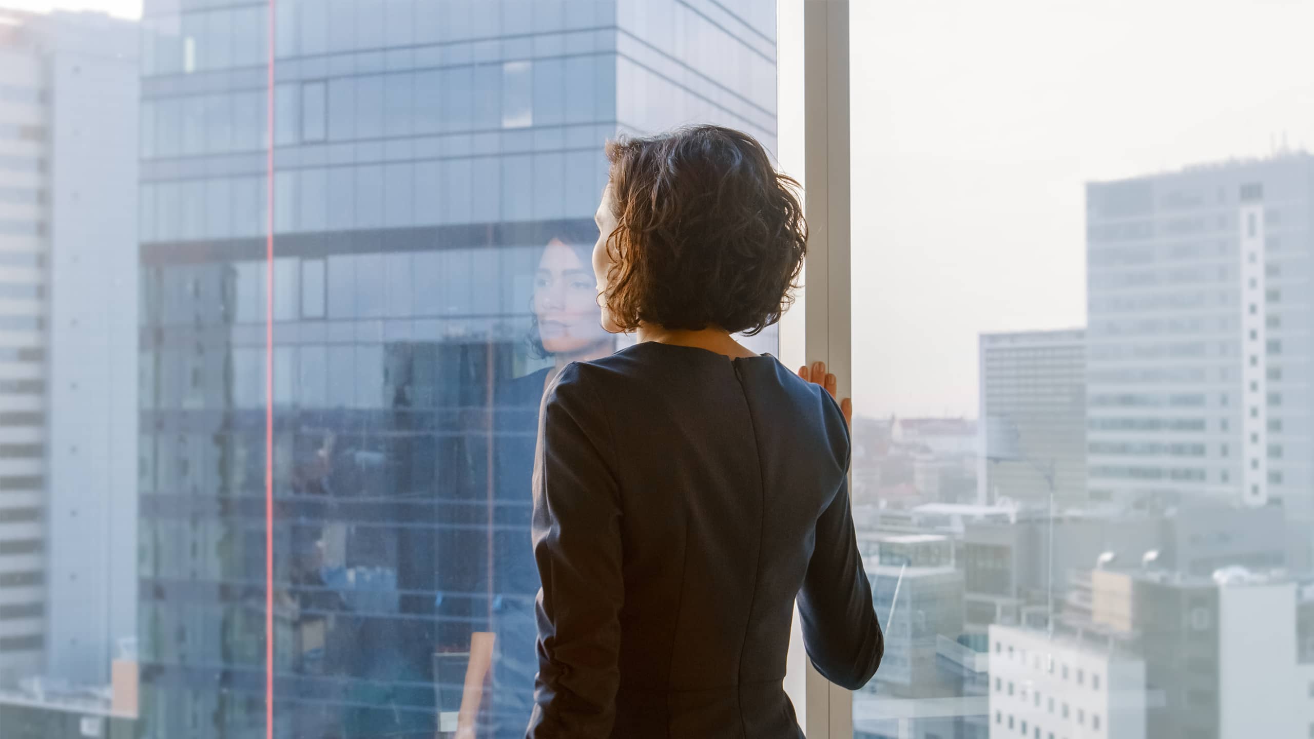 Symbolbild zum message.TALKS Frauen in Spitzenpositionen: Eine Businessfrau blickt aus dem Bürofenster auf die Skyline.