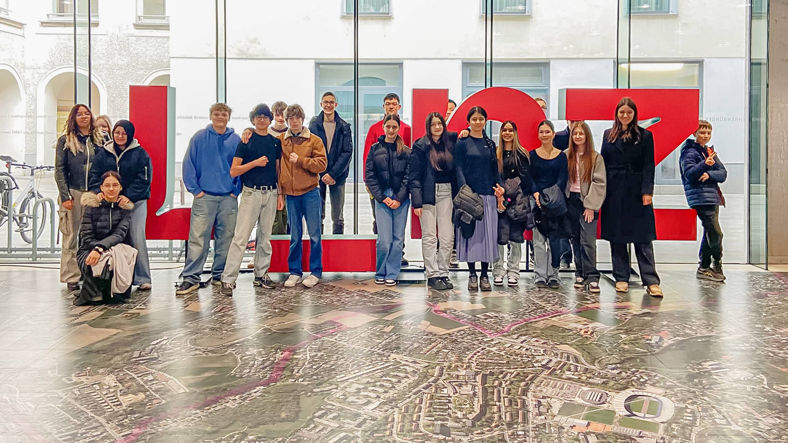 Gruppe Jugendlicher bei einer Beteiligungsaktion im Rathaus Linz, stehend vor dem roten LINZ-Schriftzug – Symbolbild für gelebte Jugendpartizipation in Linz und aktive Einbindung junger Menschen in Stadtentwicklung.