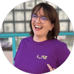 Porträt einer lachenden Silvia Hackl mit Brille im violetten T-Shirt mit gelbem „Linz“-Logo