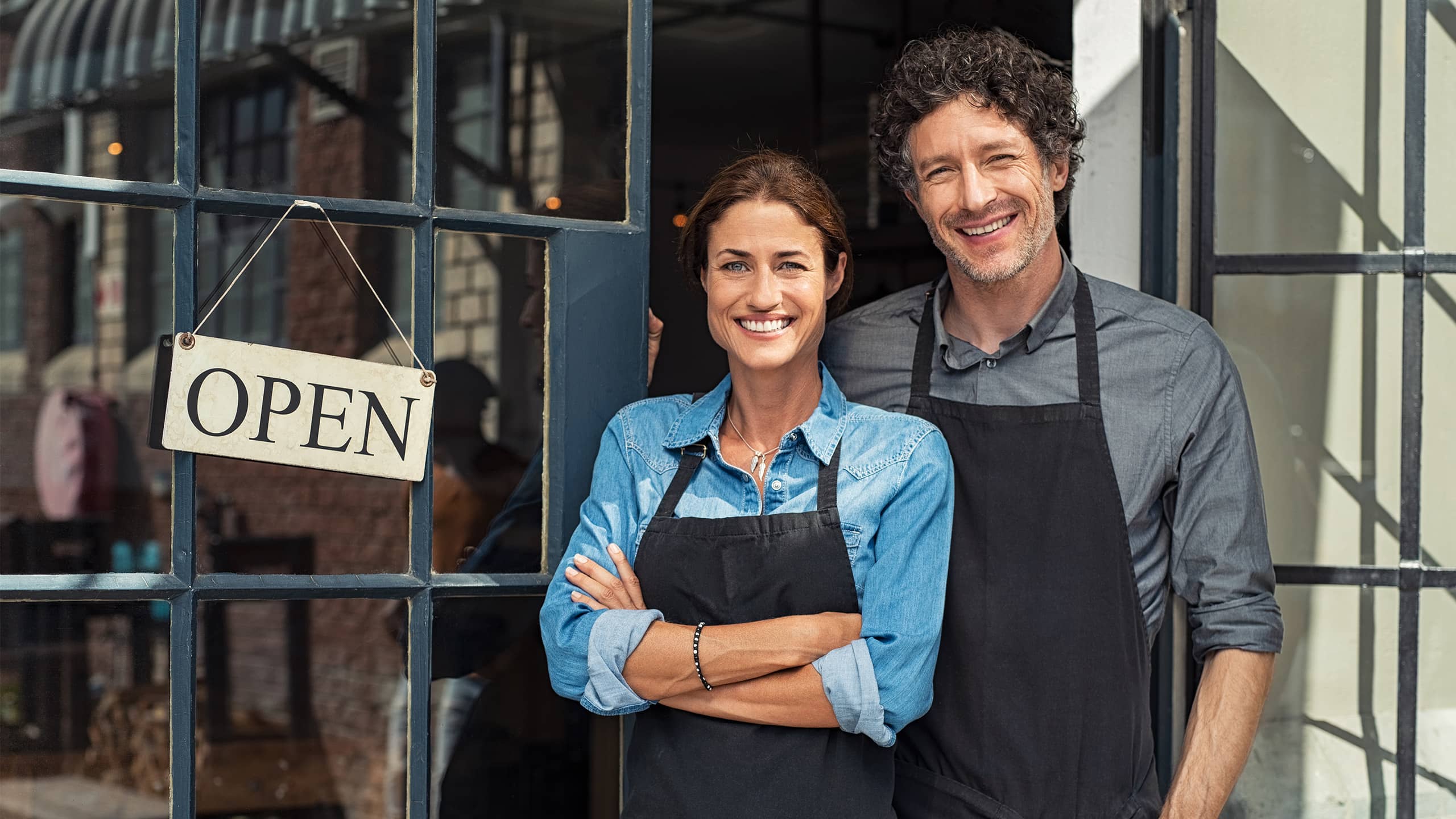 Zwei Gründer:innen vor ihrem neu eröffneten Geschäft, lächelnd im Eingangsbereich mit „Open“-Schild – Symbolbild für erfolgreiche Ansiedlung durch gezieltes Standortmarketing und eine überzeugende Standortwebsite.