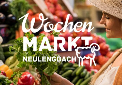 Frau mit Strohhut hält frische Kräuter vor einer Gemüseauslage am Wochenmarkt Neulengbach. Im Vordergrund ist das Marktlogo mit Schaf und Schriftzug prominent zu sehen.